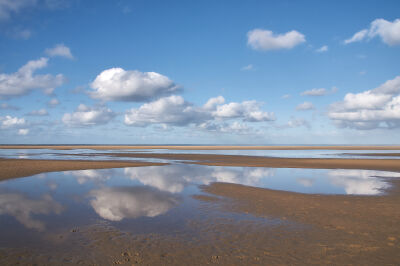 Wolken weerspiegelen in het water op het strand