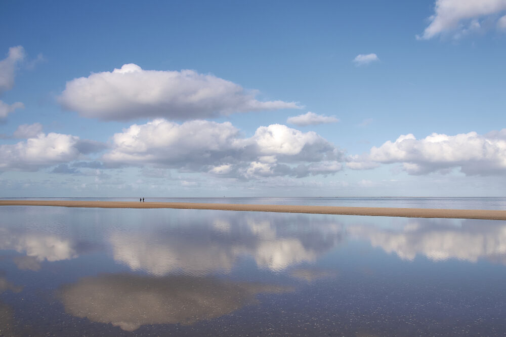 Wolken weerspiegelen in het water op het strand