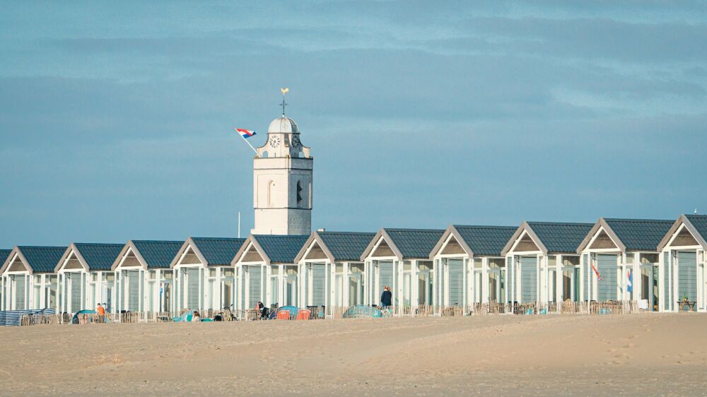 Witte strandhuisjes en kerktoren langs te skyline van Katwijk aan zee