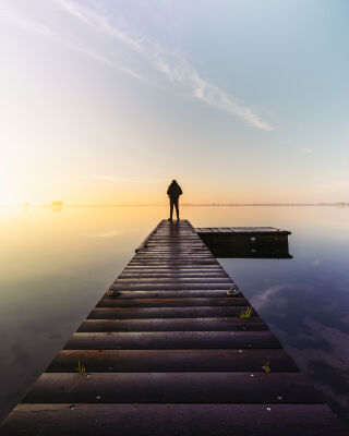 Silhouette Standing On A Jetty During Golden Hour Mist